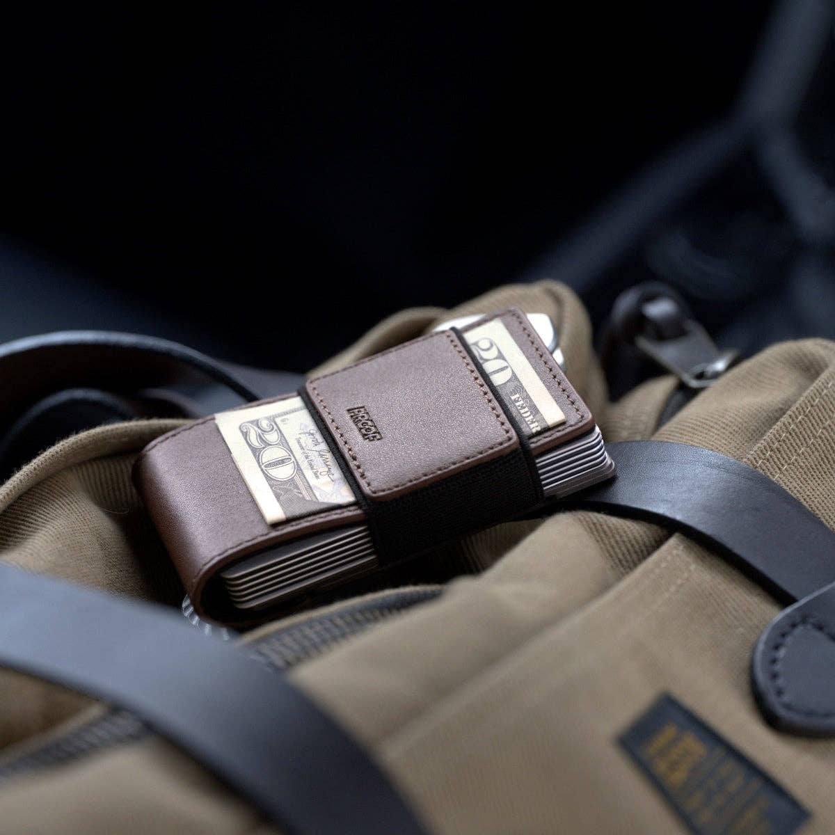PROOF Legacy wallet holding folded bills under its strap, resting on a khaki canvas bag