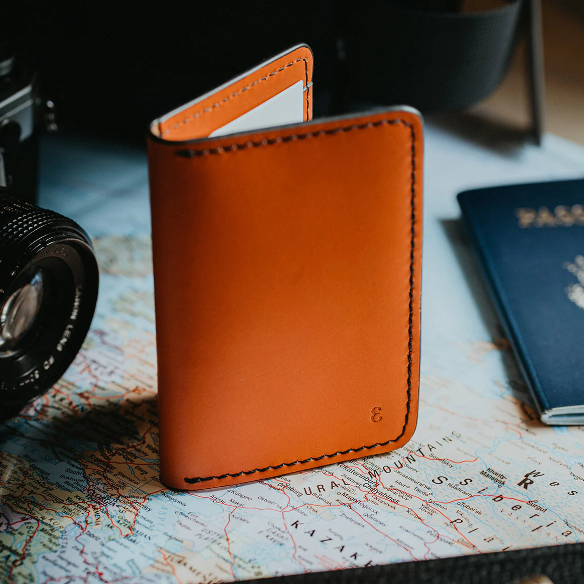 High-quality men's everyday carry items, including a brown leather wallet, a map, and a camera, arranged on a desk.