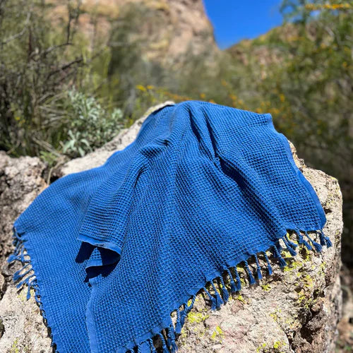 A blue Turkish beach towel draped over a sand dune, set against a serene beach backdrop.