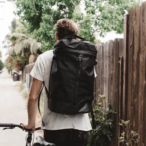 A stylish black travel backpack surrounded by everyday carry items in an urban setting.