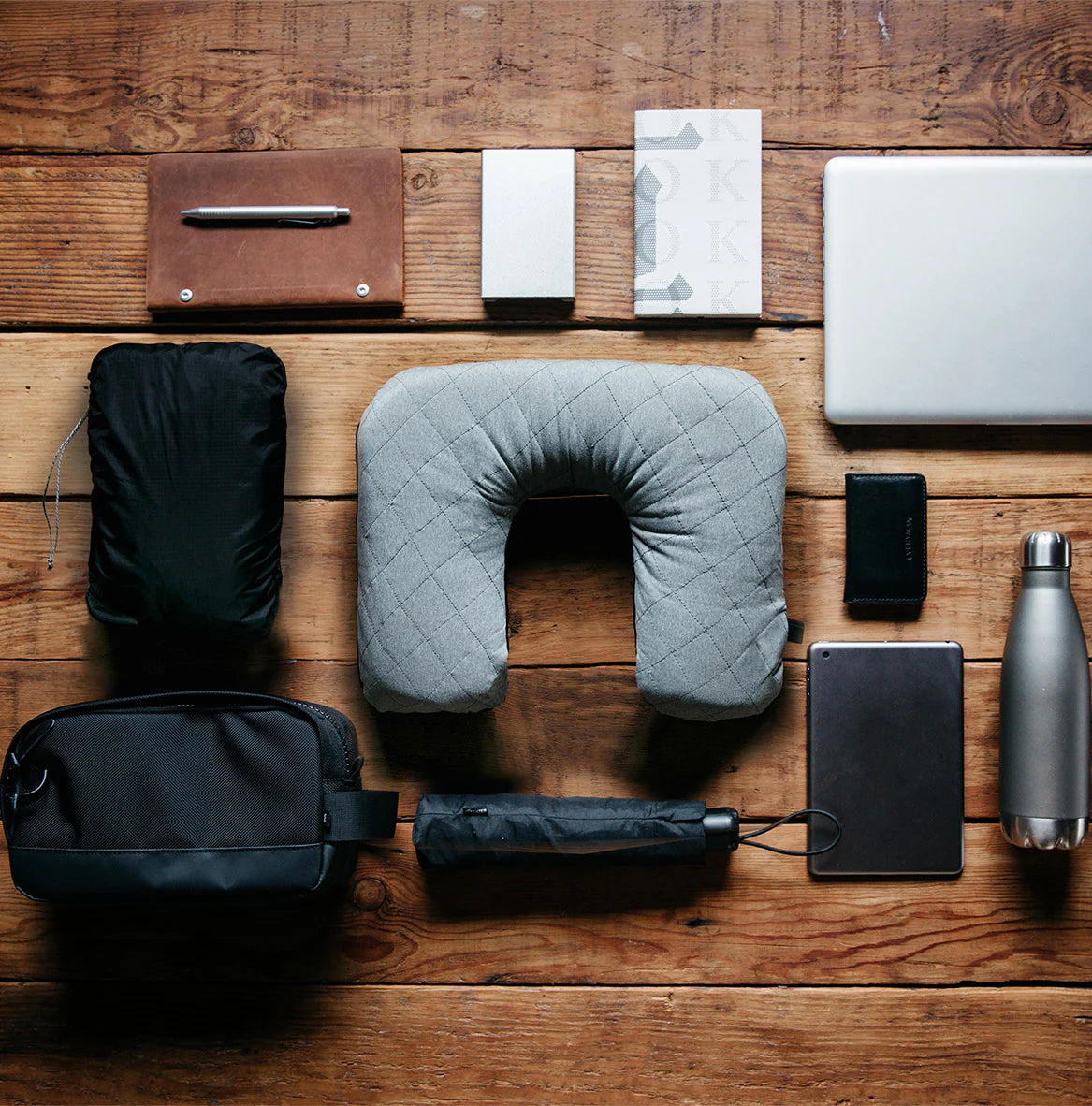 A stylish travel pillow with a sleek cover, surrounded by a Grafton Pen, Holden Wallet, multitool, and a Hideout Dopp Kit, set in a minimalist table.