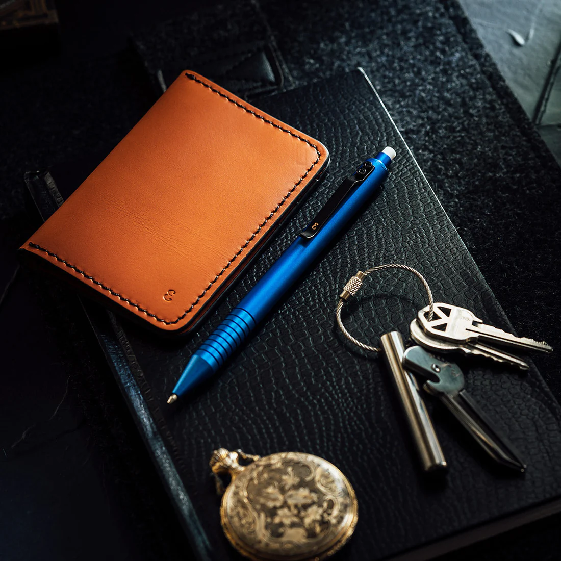 Every day carry wallet, pen, and keyring on a black desk.