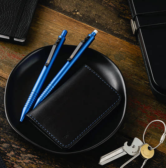 Aegean Blue Grafton pen and matching mechanical pencil on a black dish beside a black Holden Card Wallet stitched in blue, with a Porter Key on a steel cable key ring