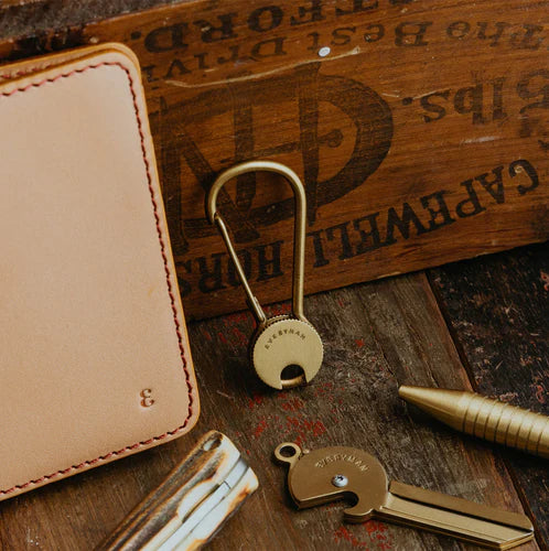 Flat lay of high-quality everyday carry items for men, including a Grafton Pen and Pencil set, Holden Wallet, multitool, minimalist keychain, on a wooden surface.