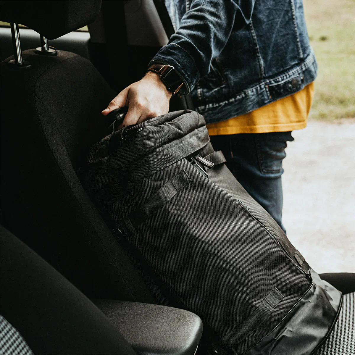 A stylish backpack inside a car, filled with everyday carry items, set against a black seat in a car.