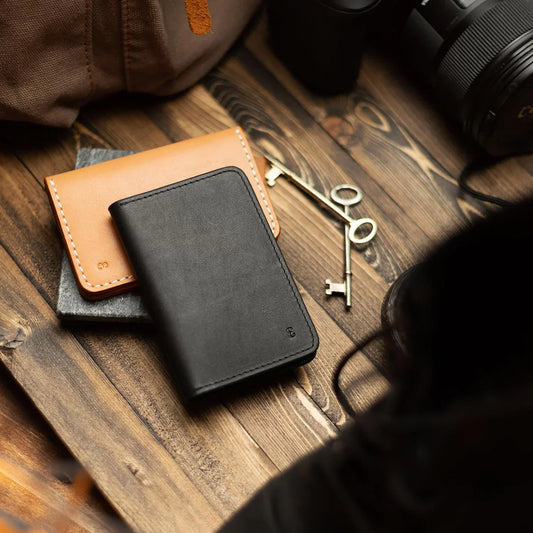 Two leather bifold wallet and two keys arranged on a wooden surface.