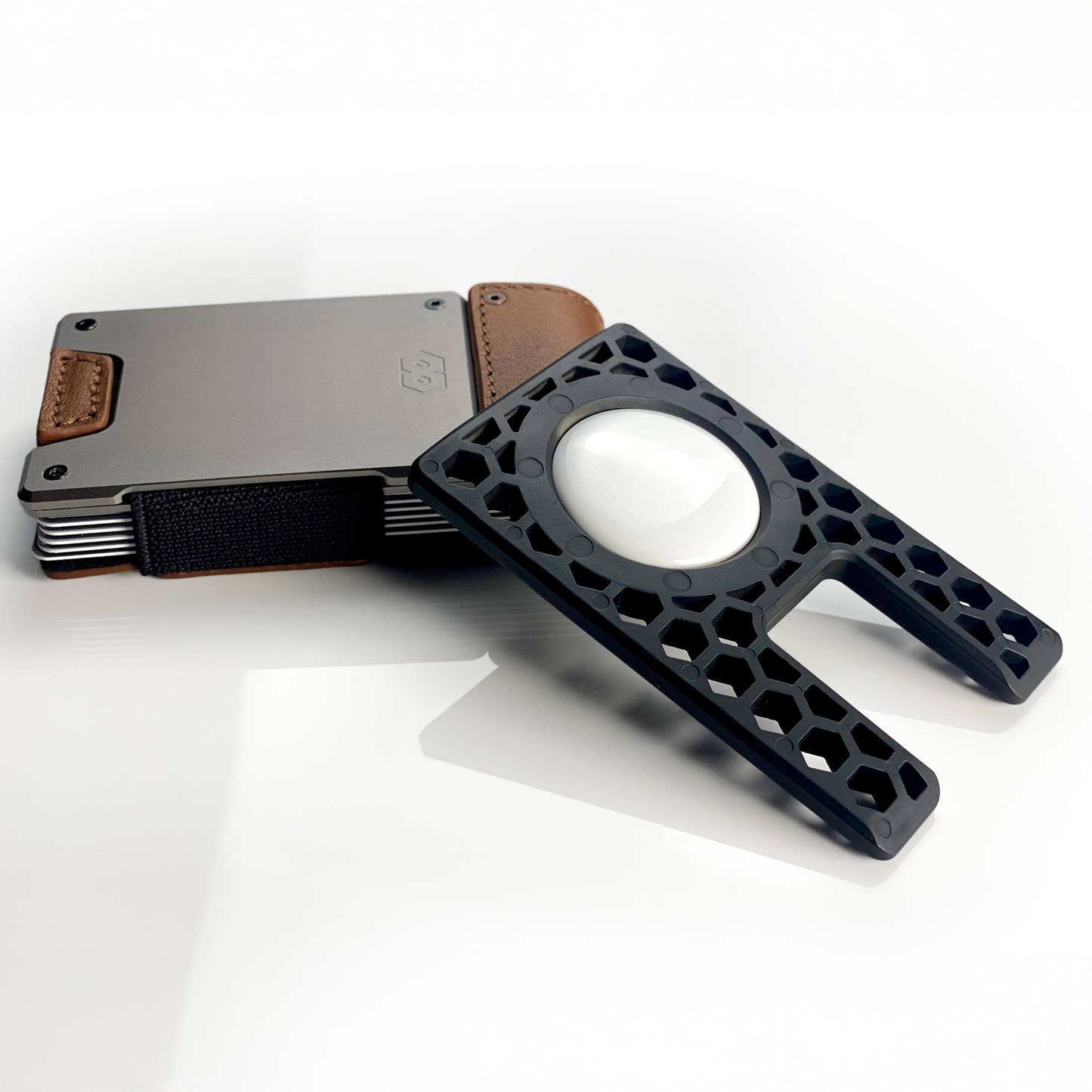 PROOF AirTag holder leaning against a satin gunmetal PROOF wallet, AirTag seated in the outer face of the frame