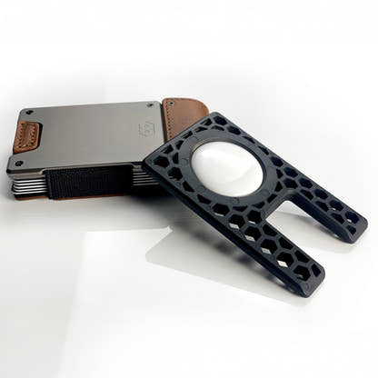 PROOF AirTag holder leaning against a satin gunmetal PROOF wallet, AirTag seated in the outer face of the frame