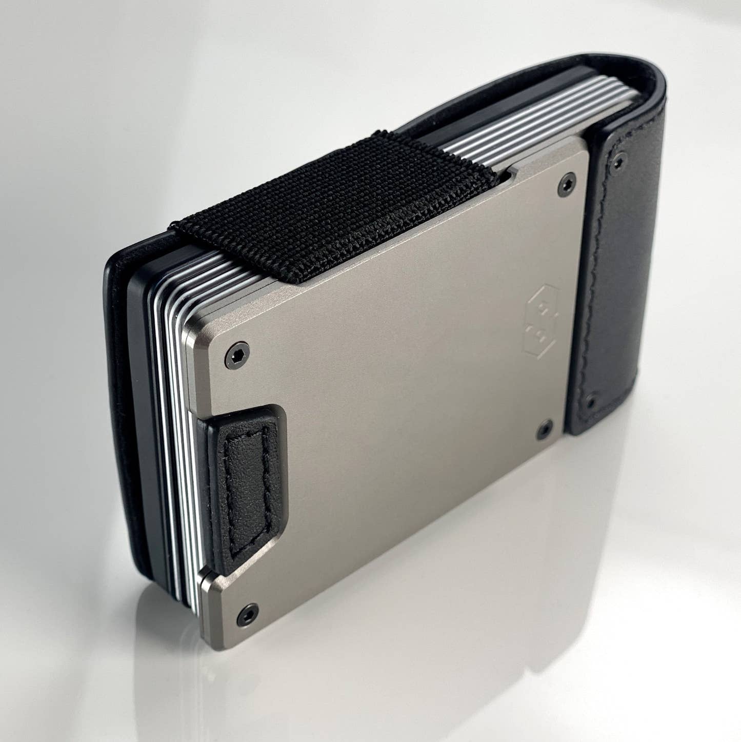 Side view of a satin gunmetal PROOF wallet with black leather straps packed with cards under its elastic band; the AirTag holder itself is not visible in this frame
