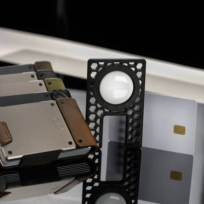 PROOF AirTag holder with an AirTag seated, standing upright beside two payment cards and a stack of PROOF wallets