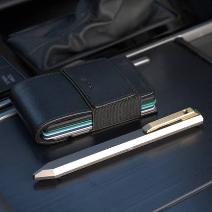 PROOF Vanguard pen on brushed dark metal beside a black PROOF wallet loaded with cards
