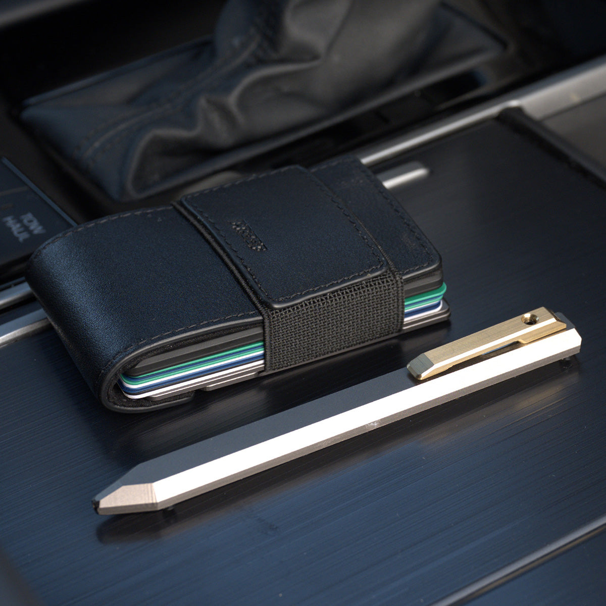 PROOF Vanguard pen on brushed dark metal beside a black PROOF wallet loaded with cards