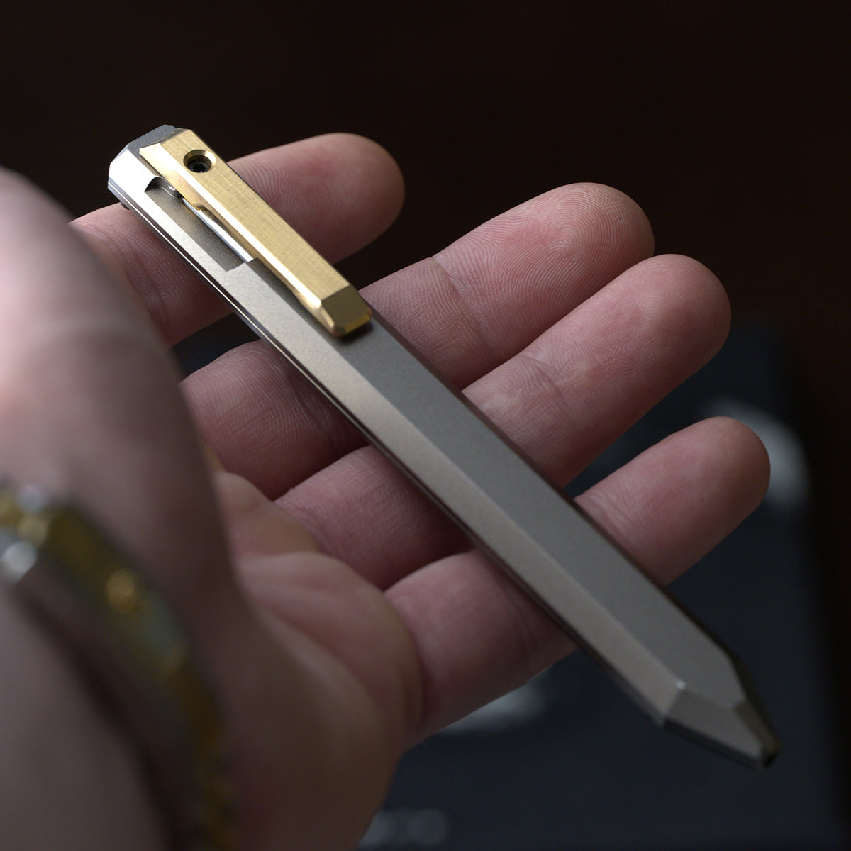 PROOF Vanguard pen held horizontally in a hand, showing the length of the faceted satin barrel and the brass bolt-action clip