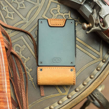 Top-down view of the PROOF Executive wallet on a studded leather surface beside antique brass hardware, gunmetal plate and tobacco leather strap facing up