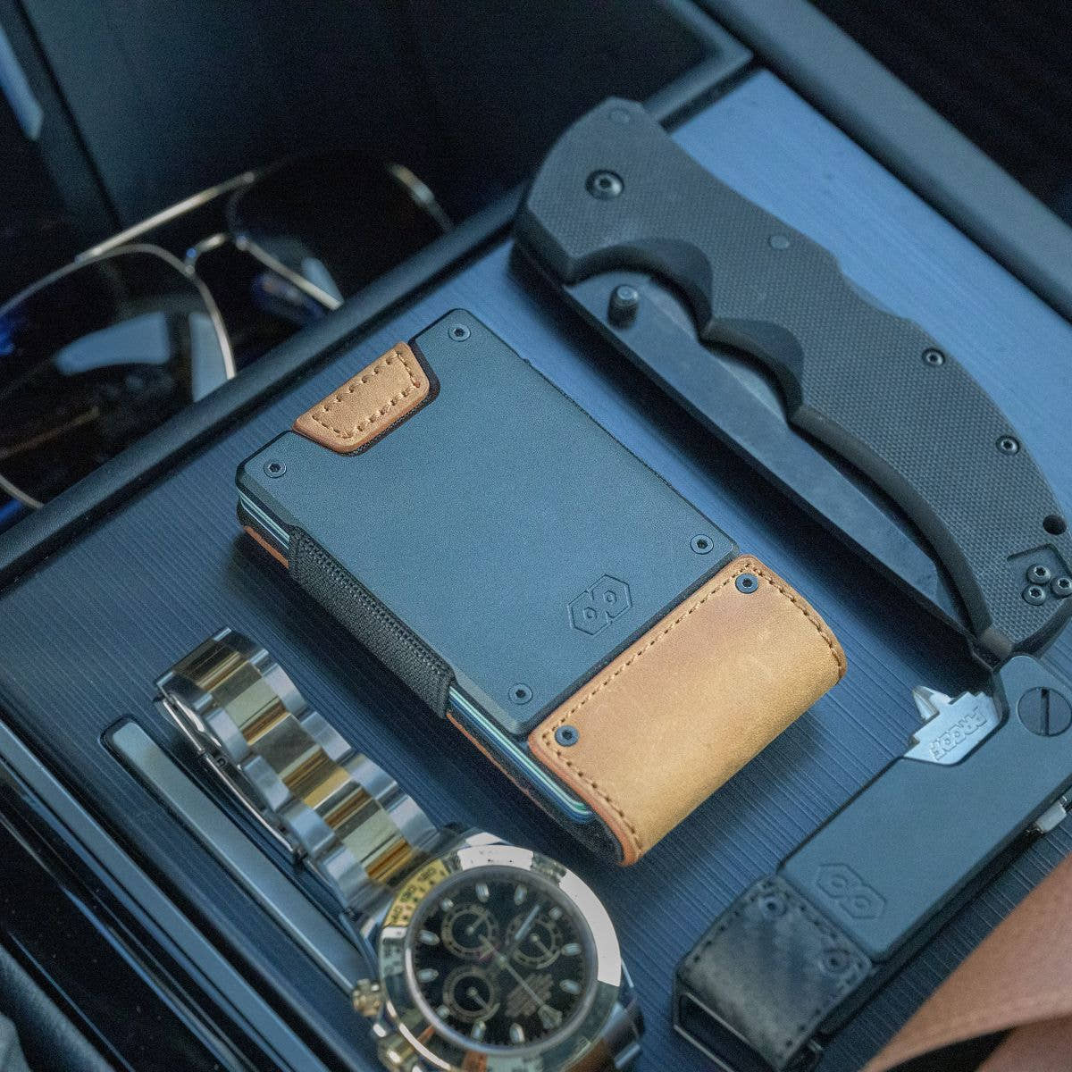 PROOF Executive wallet in tobacco leather resting on a car console beside a wristwatch, folding knife and sunglasses