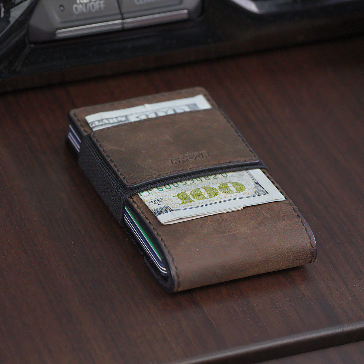 PROOF Founder wallet in bomber leather on a wood console, $100 bills held under the elastic cash strap