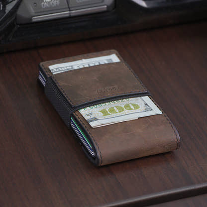 PROOF Founder wallet in bomber leather on a wood console, $100 bills held under the elastic cash strap