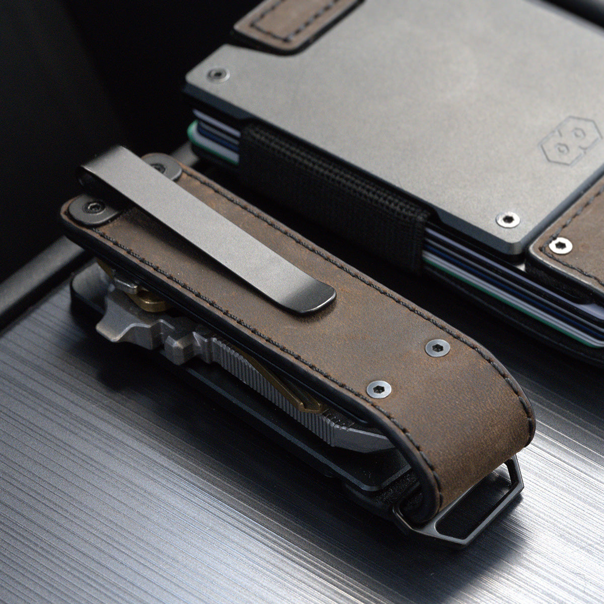 Back of the PROOF Founder key holder on dark wood, steel pocket clip over the brown leather panel, leaning against a PROOF wallet