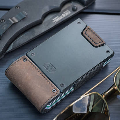 PROOF Founder wallet on a car dashboard beside a folding knife and gold aviator sunglasses