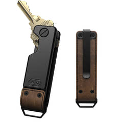 PROOF Founder key holder front and back: dark gunmetal aluminum body with brass keys fanned from the pivot, and a brown top-grain leather back panel with pocket clip and steel loop