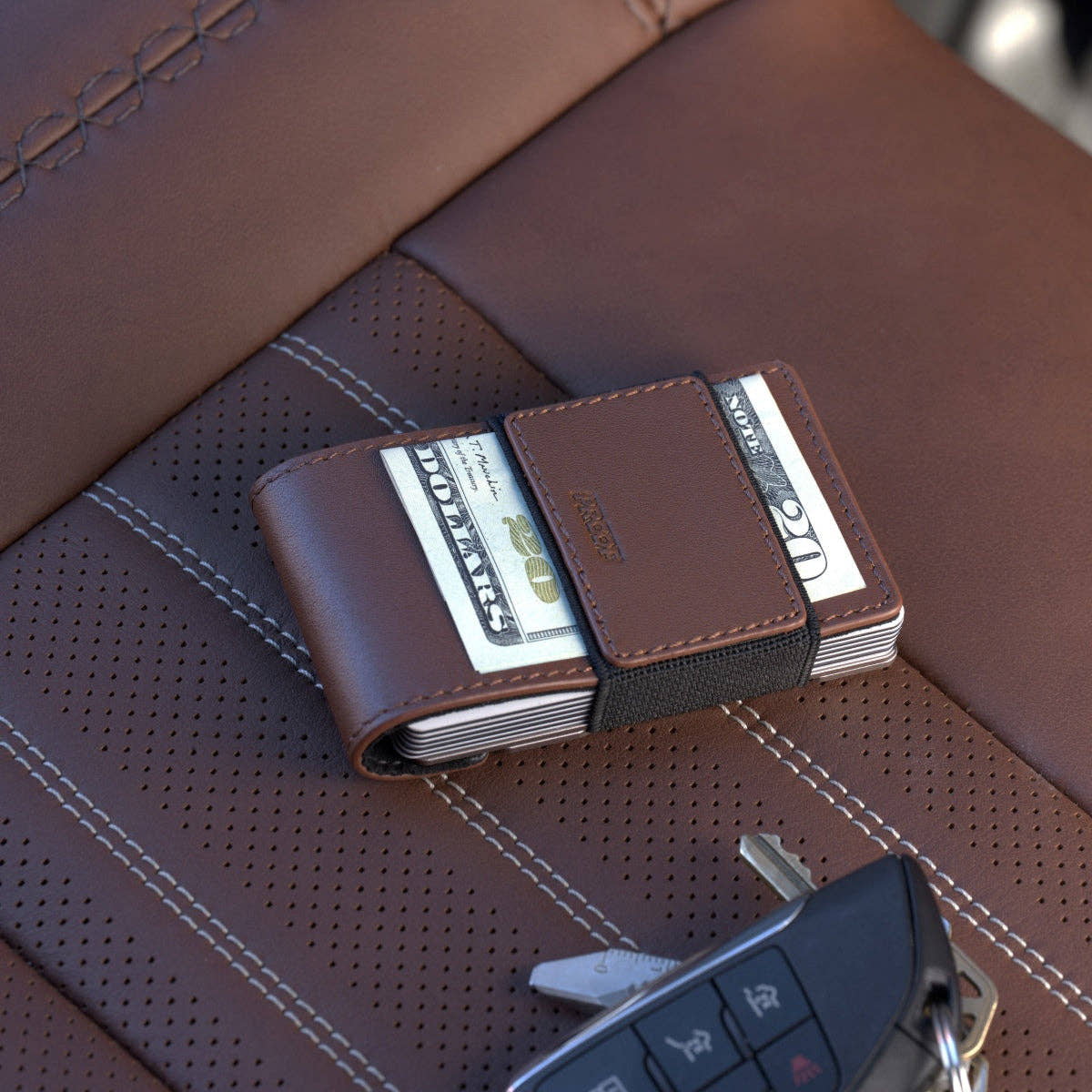 PROOF Legacy wallet on a brown perforated leather car seat with cash under its strap and a key fob alongside
