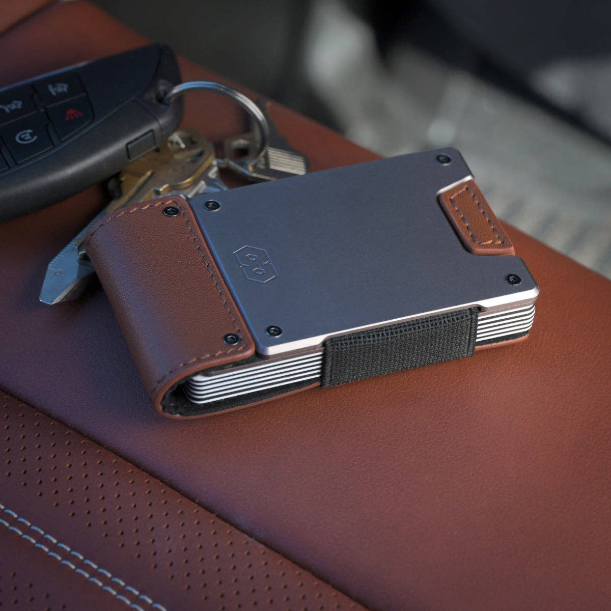 PROOF Legacy wallet resting on a brown leather car seat next to a key fob, satin gunmetal plate and burnished oak leather in view