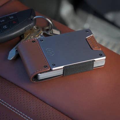 PROOF Legacy wallet resting on a brown leather car seat next to a key fob, satin gunmetal plate and burnished oak leather in view