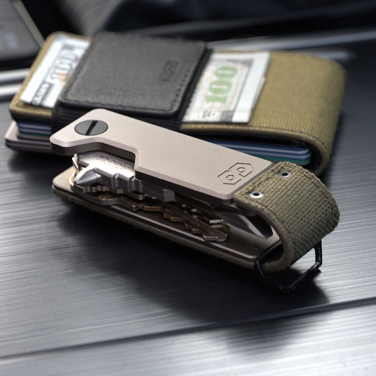 PROOF Operator key holder open on brushed metal in front of a PROOF wallet holding folded bills under its elastic strap