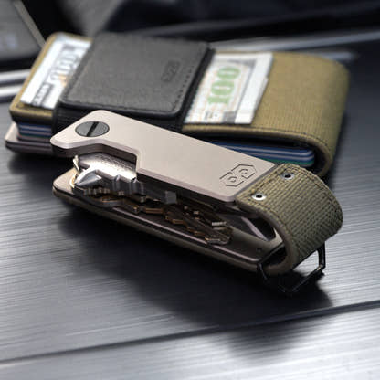 PROOF Operator key holder open on brushed metal in front of a PROOF wallet holding folded bills under its elastic strap