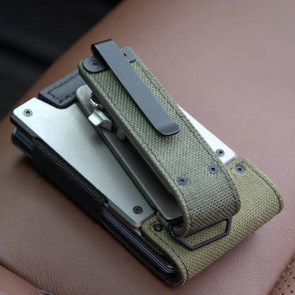 Back of the PROOF Operator key holder on a tan leather car seat, black pocket clip mounted over the olive drab nylon panel