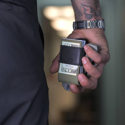 Man holding the PROOF Operator wallet with cash and cards gripped under the strap, wristwatch and tattooed forearm in frame