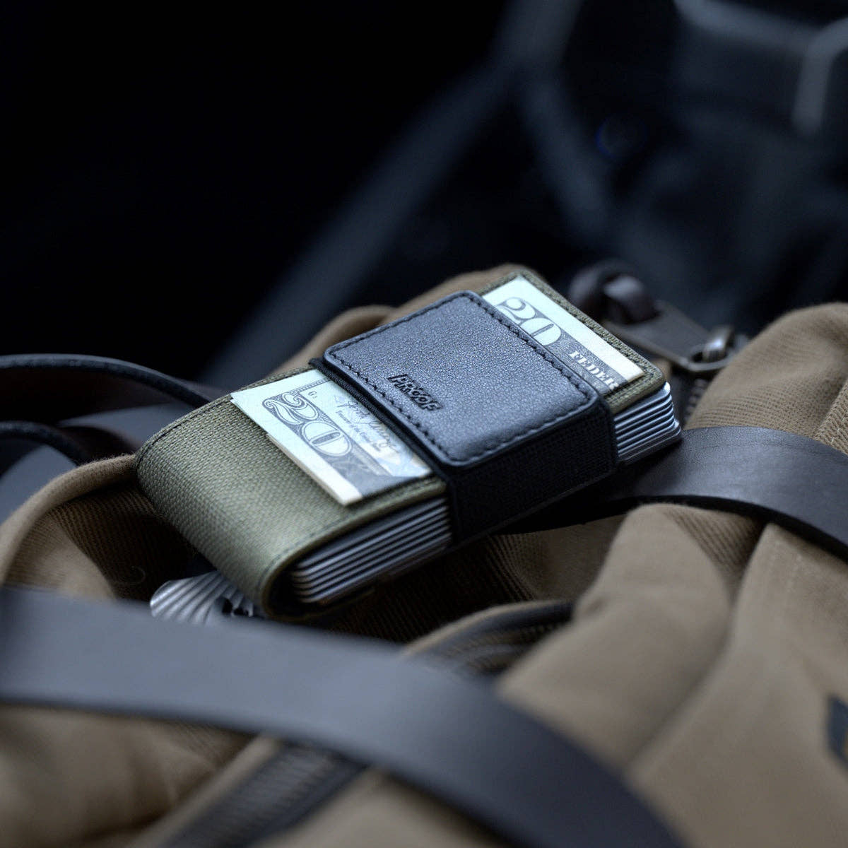 PROOF Operator wallet with bills under its black leather strap, resting on a khaki canvas bag