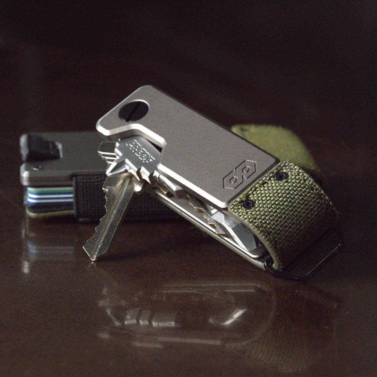PROOF Operator key holder with keys fanned out on a dark reflective surface, a PROOF wallet with stacked cards behind it
