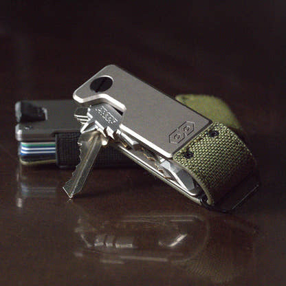 PROOF Operator key holder with keys fanned out on a dark reflective surface, a PROOF wallet with stacked cards behind it