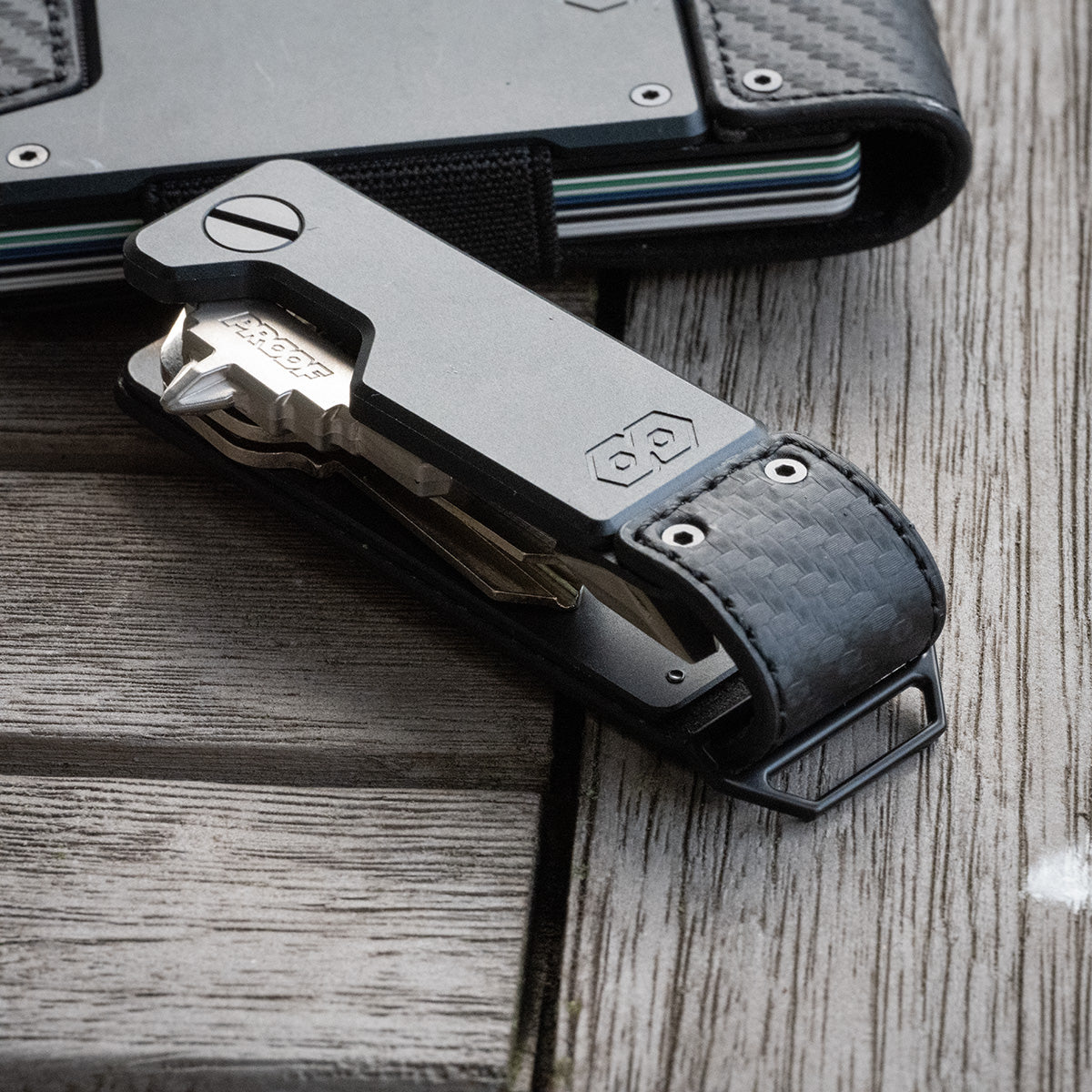 PROOF Oracle key holder leaning against a matching carbon fiber PROOF wallet on weathered wood planks, keys and multi-tool partly deployed