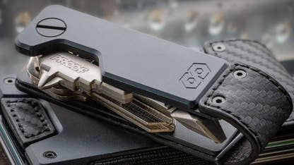 Close-up of the PROOF Oracle key holder with its keys splayed open, carbon fiber weave and gunmetal plate sharp against a blurred background