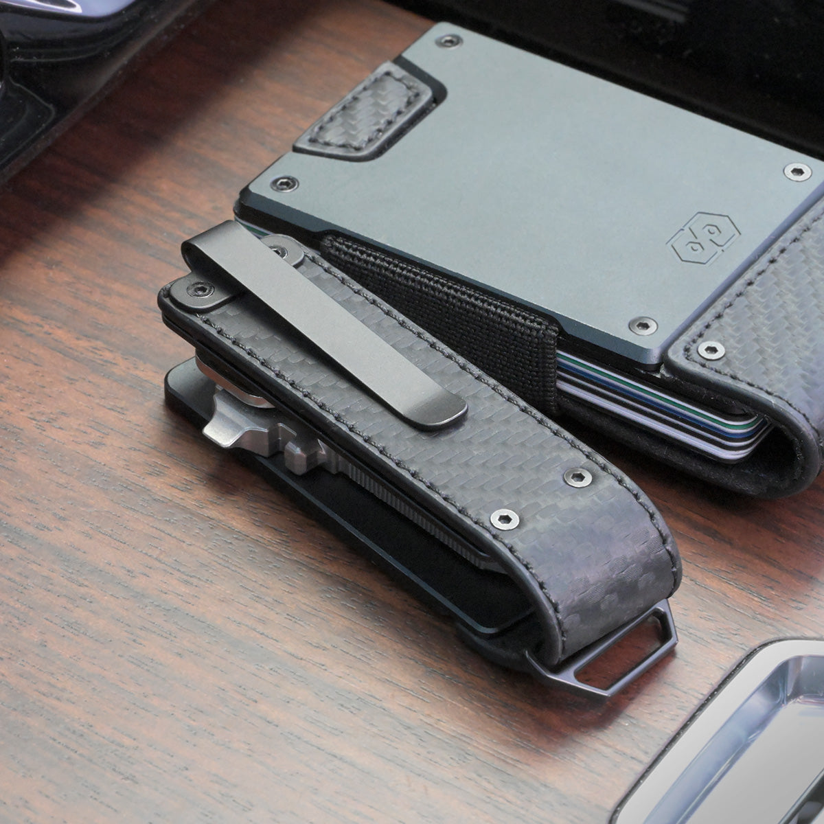 Back of the PROOF Oracle key holder on a wood surface, steel pocket clip mounted over the carbon fiber panel, resting against a PROOF wallet