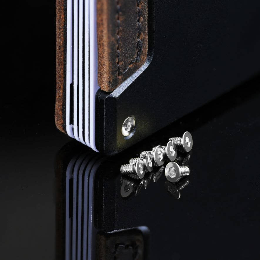 Nickel PROOF wallet bolts on a dark reflective surface beside a wallet corner fitted with a matching nickel bolt