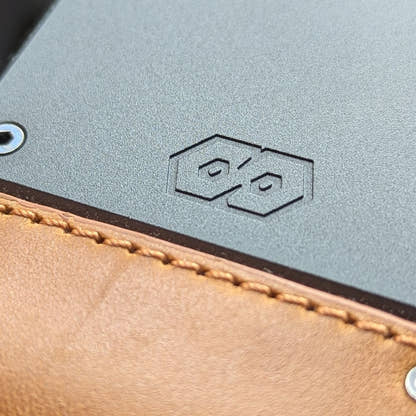 Close-up of the PROOF Executive's gunmetal aluminum plate with embossed hexagon logo above tobacco leather