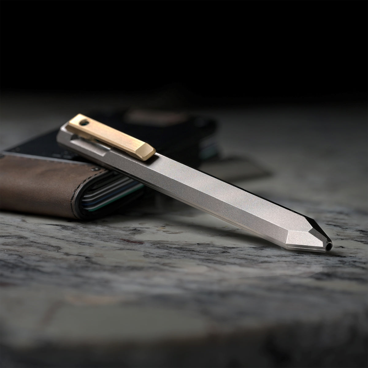 PROOF Vanguard pen lying on dark weathered wood beside a brown leather PROOF wallet