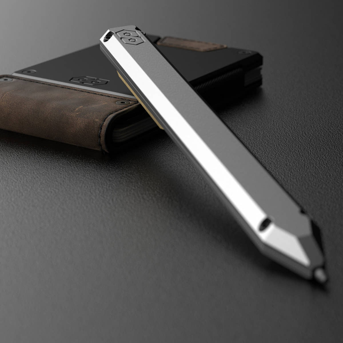 PROOF Vanguard pen propped against a PROOF wallet in brown leather, the embossed hexagon logo visible on the pen's end cap