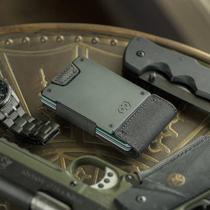 PROOF Monolith wallet on an engraved metal tray with a folding knife and steel watch, black nylon strap in the foreground