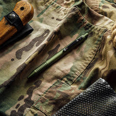 OD Green Super Matte Grafton pen on camo fabric beside a fixed-blade knife